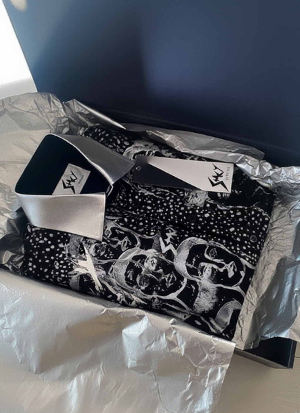 Stacy Stewart Smith Men’s Pawns in Silver on Black Hand-Painted Premium Cotton Percale Dress Shirt folded in a black giift box with gold tissue paper and brand label and tag showing on a light colored surface. 