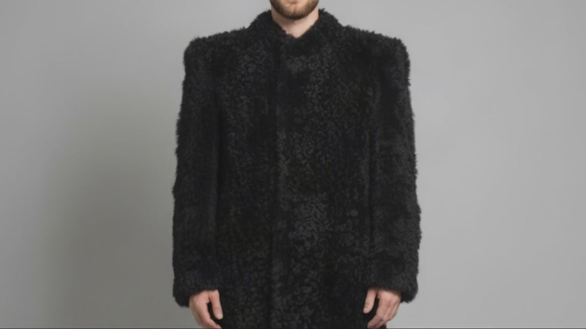Man wearing the black Bishop Tigrado shearling coat opens the front to reveal its satin lining, interior pockets, and a hand-painted shirt.
