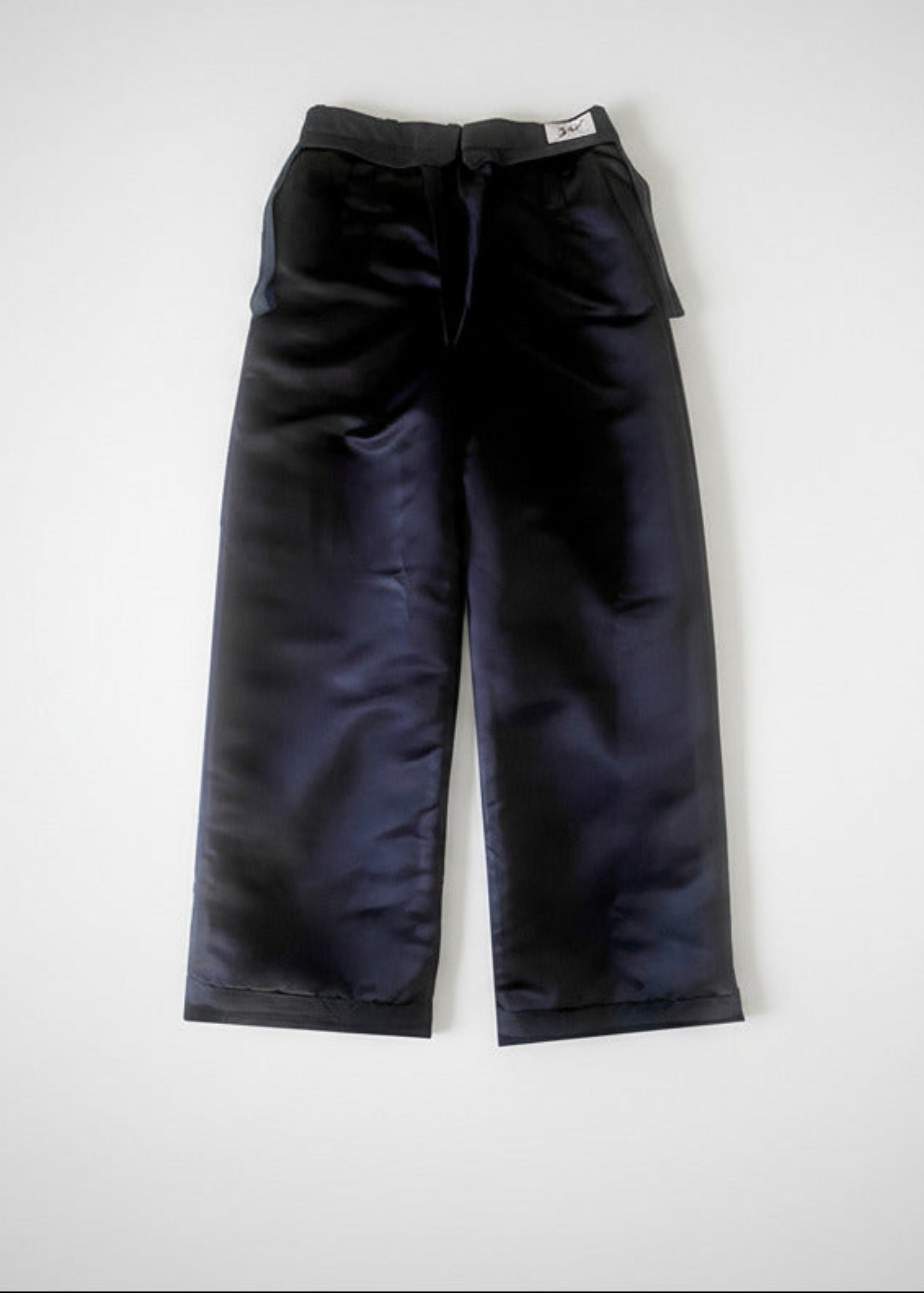 Stacy Stewart Smith Men's Suede Pleated Windsor Pants on a surface back inside lining view with brand label on a white backdrop.